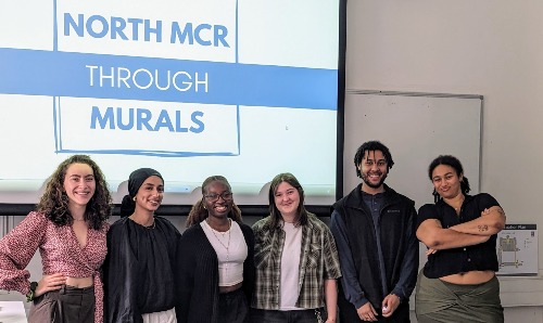 Six student interns standing in front of North MCR through murals presentation.